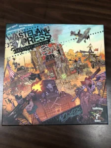 An image of a colorful board game cover titled "Wasteland Express Delivery Service" by Matt Riddle and Ben Pinchback, designed by Jonathan Gilmour; artwork depicts a chaotic, post-apocalyptic landscape with vehicles, graffiti, and fantastical creatures. The logo of Pandasaurus Games is displayed at the bottom right corner.