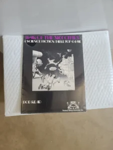 A tabletop game titled "WAR OF THE SKY CITIES" by Bob McLeod, displayed on a flat surface with bubble wrap to its left. The cover features monochrome artwork of a futuristic battle with robots and spaceships. The game is produced by Fantasy Games Unlimited Inc.