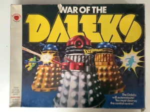 A worn vintage board game box titled "WAR OF THE DALEKS," featuring two Daleks with word "EXTERMINATE" and battle effects. The box includes text "A fast exciting all action game" and branding logos.
