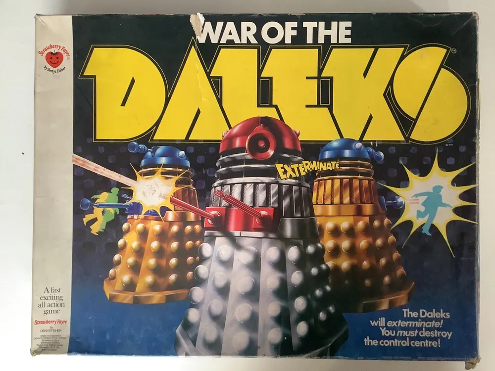 A worn vintage board game box titled "WAR OF THE DALEKS," featuring two Daleks with word "EXTERMINATE" and battle effects. The box includes text "A fast exciting all action game" and branding logos.