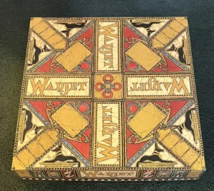 Ornate, square board game box with "WADJET" text, Egyptian-themed illustrations, and vibrant red, gold, and blue colors on a textured black background.