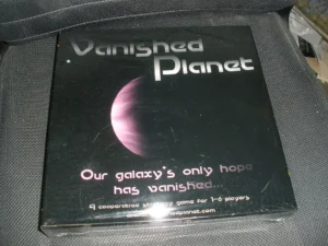 A photo of the boxed board game "Vanished Planet" placed on a dark fabric surface. The box features an image of a planet with the text "Our galaxy's only hope has vanished. A cooperative strategy game for 1-6 players. www.vanishedplanet.com".