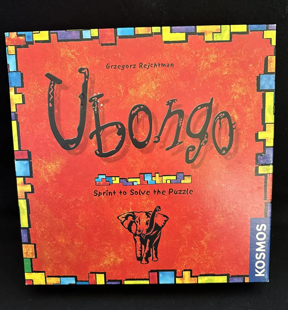 A photo of the board game "Ubongo" by Grzegorz Rejchtman with the tagline "Sprint to Solve the Puzzle", published by KOSMOS, displayed against a black background. The box cover features a colorful red and orange design with puzzle pieces along the border.