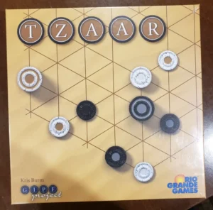 A board game named "TZAAR" from the GIPF project series by Kris Burm, produced by Rio Grande Games, with black and white pieces on a grid-patterned board.