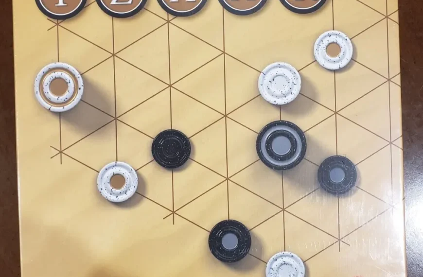 A board game named "TZAAR" from the GIPF project series by Kris Burm, produced by Rio Grande Games, with black and white pieces on a grid-patterned board.