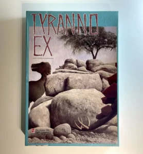 Alt text: Book cover of "TYRANNO EX," featuring a landscape of rocky terrain and a lone tree, with a partial view of a dinosaur figure peeking from behind large stones. The logo of The Avalon Hill Game Company appears in the bottom left corner.