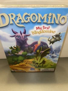 A sealed board game box for "Dragomino: My first Kingdomino" with colorful cartoon dragons and a fantasy landscape illustrated on the cover.