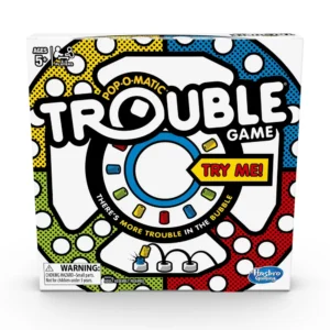 A box of the "Trouble" board game by Hasbro Gaming, featuring a colorful pop-o-matic bubble in the center, the words "There's more TROUBLE in the bubble," and a "Try Me!" sticker on the corner, indicating interactive packaging. The game is suitable for ages 5 and up and for 2-4 players, with a choking hazard warning for small parts not for children under 3 years.