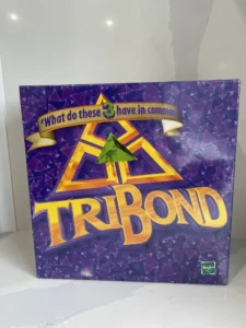 A "Tribond" board game box with the tagline "What do these 3 have in common" displayed on a purple geometric pattern background, placed on a marble surface.