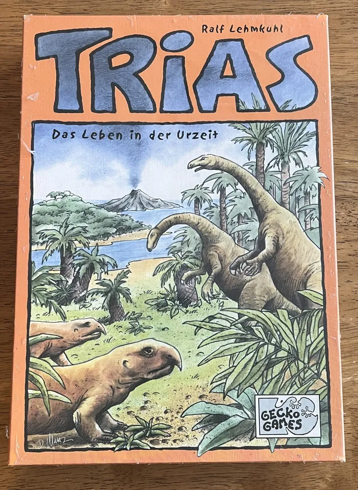 A book cover with the title "TRIAS" in large letters at the top and the subtitle "Das Leben in der Urzeit" beneath it. The illustration depicts a prehistoric scene with dinosaurs and lush vegetation, with a volcano in the background. The author's name, Ralf Lehmkuhl, is at the top, and a "GECKO GAMES" logo is at the bottom right.