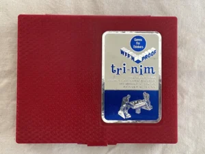 Vintage "Tri-Nim" game box, by Bruce L. Hicks and Hervey G. Hicks, with a graphic of two people playing a game, resting on a red surface with a textured pattern.