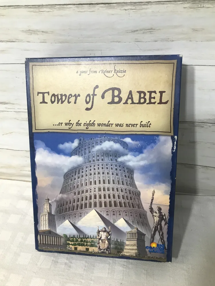 Board game titled "Tower of Babel" by Reiner Knizia displayed on a wooden background. The cover features an illustration of the Tower of Babel among various other wonders of the world, like the Pyramids of Giza and the Colossus of Rhodes.