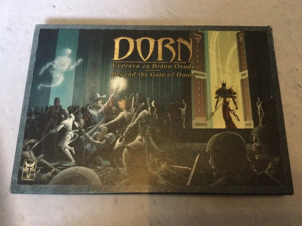 A tabletop game box titled "DORN: Výprava za Bránou Osudu / Beyond the Gate of Doom," featuring fantasy artwork with warriors fighting skeletons in front of a large gate where a spectral figure and a character holding a staff appear.