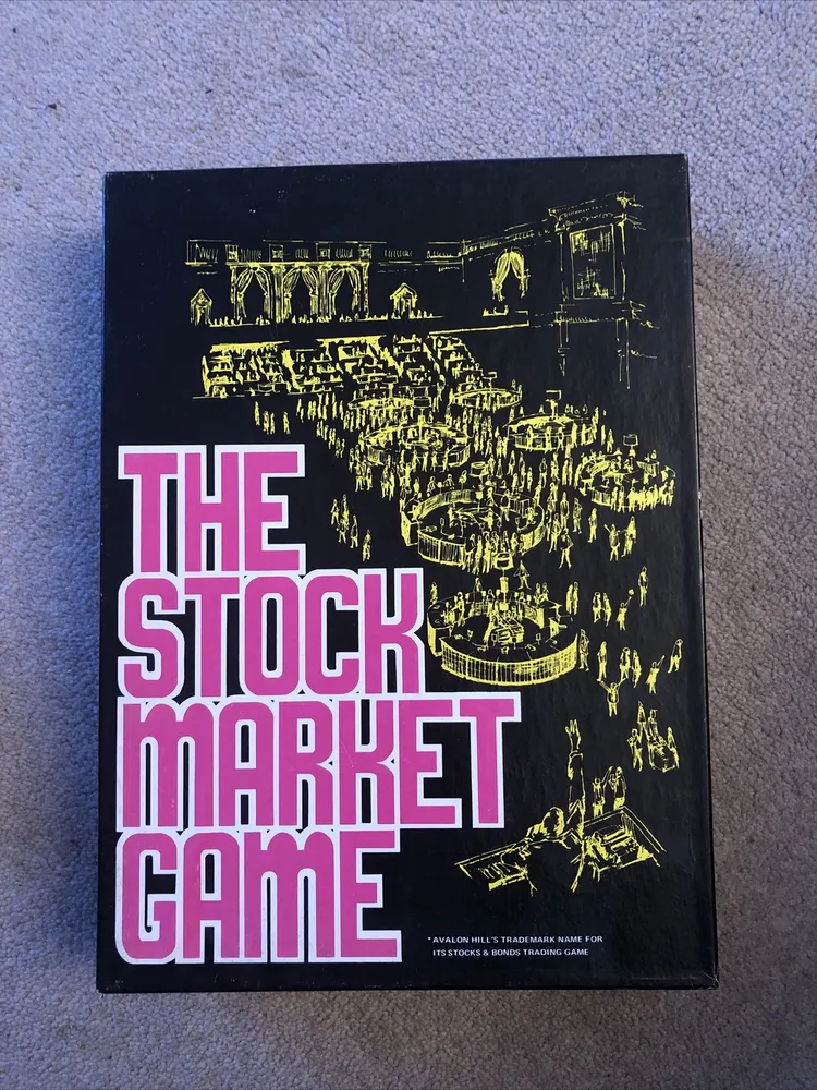 A photo of "The Stock Market Game" board game box with yellow illustrations of a stock exchange scene on a black background and pink title text.