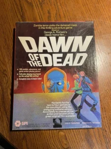 An old "Dawn of the Dead" board game box featuring a large title, an illustration of a male and female character fending off a blue-faced zombie, and promotional text about the game's features and the film it's based on. The box shows signs of wear and is placed on a wooden surface.