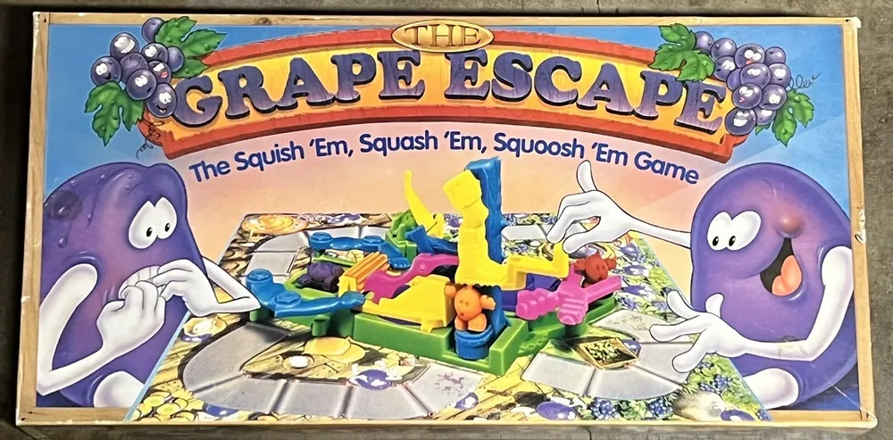 Board game cover for "The Grape Escape" featuring two cartoonish purple grapes with faces and arms, one on each side, looking at plastic game pieces and a game board with playing areas and traps. The tagline reads "The Squish 'Em, Squash 'Em, Squoosh 'Em Game."