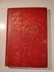A worn red hardcover book with the title "The Game of Logic" in gold cursive lettering.