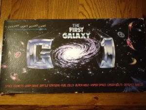 Board game box titled "The First Galaxy 1" featuring space-themed graphics including a spiral galaxy, spaceships, and game features listed as space rockets, warp drive, battle stations, fuel cells, black hole, hyper space, laser bolts, and defense shield.