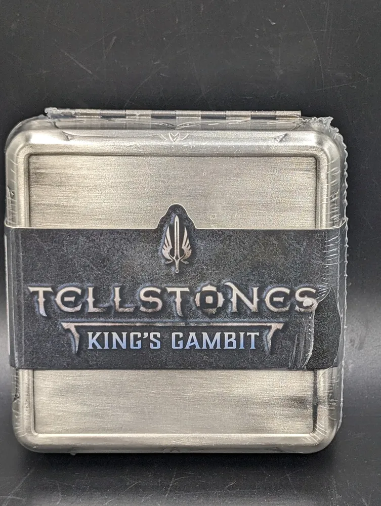 A metal tin with the embossed text "TELLSTONES KING'S GAMBIT" secured with a black rubber band, against a black background.