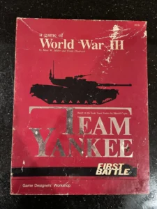 A worn board game box cover titled "Team Yankee First Battle," with a silhouetted tank graphic, indicating a World War III theme, based on the book Team Yankee by Harold Coyle, by Game Designers' Workshop.