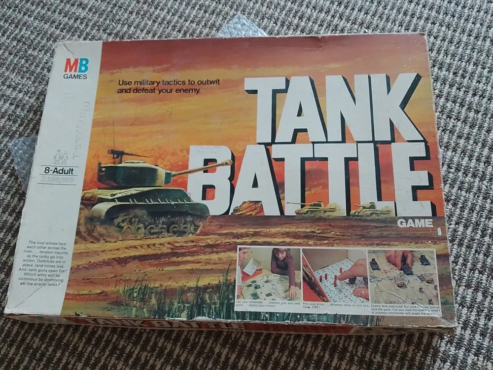 A worn "Tank Battle" board game box by MB Games for ages 8-adult, featuring images of tanks and gameplay with an orange and sunset sky background.