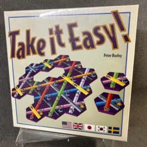 Board game cover titled "Take it Easy!" by Peter Burley, featuring hexagonal tiles with colorful lines and numbers, and flags from various countries along the bottom edge.