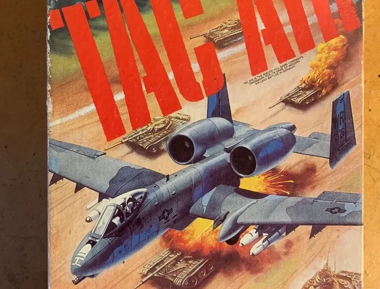 Alt text: An image of a vintage board game cover titled "Tac Air – The Game of Modern Air-Land Battles in Germany", published by The Avalon Hill Game Company. The artwork depicts a military jet in the foreground with tanks on the ground below engaging in combat.