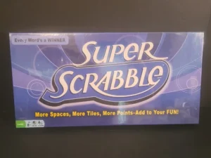 A sealed "Super Scrabble" board game box displaying the text "Every Word's a WINNER" and "More Spaces, More Tiles, More Points-Add to Your FUN!" with age recommendation "8+" and "2-4 players" icons at the bottom left corner.