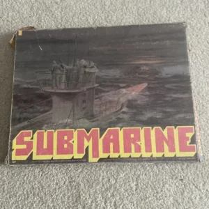 A worn board game box titled "SUBMARINE" with an illustration of a submarine and sailors on its cover, placed on a carpeted floor.