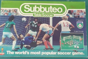 Box cover for "Subbuteo Table Soccer," depicting a dynamic illustrated soccer match scene with players in different colored kits and a goalkeeper diving for the ball, alongside promotional text that reads, "The world's most popular soccer game," and a small inset image displaying the miniature game setup with figures and goals.