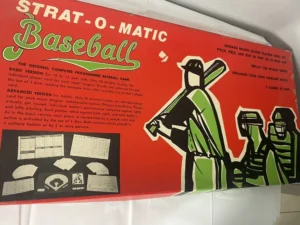 Vintage Strat-O-Matic Baseball board game box with text describing the basic and advanced versions of the game, stylized illustrations of baseball players, and images of game components.