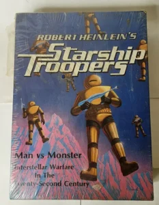 A worn copy of "Robert Heinlein's Starship Troopers" book cover featuring futuristic armored soldiers in space against a backdrop of jagged pink mountains. The cover includes the text "Man vs Monster Interstellar Warfare In The Twenty-Second Century."