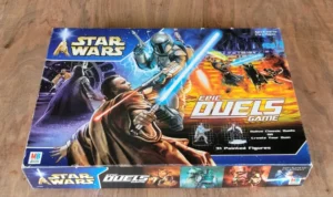 The image shows a boxed board game titled "Star Wars: Epic Duels Game" by Milton Bradley (MB) on a wooden surface. The box art features illustrations of iconic characters from the Star Wars franchise engaged in lightsaber battles, with a tagline "Relive Classic Duels or Create Your Own" and a note that the game includes 31 painted figures. The game is designed for ages 8 and up and for 2 to 6 players.