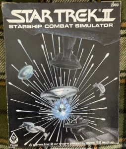Box cover of "Star Trek II Starship Combat Simulator" featuring illustrations of various Star Trek spacecraft engaged in battle, with white energy beams radiating from a central explosion, and text indicating it is a game for 2 or more players, ages 12 and up, with the FASA logo in the corner.
