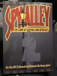 A board game titled "SPY ALLEY" with a tagline "THE GAME OF SUSPENSE AND INTRIGUE!" The cover shows a silhouette of a spy holding a briefcase with the words "TOP SECRET" and "Use Your Wit To Unmask and Eliminate the Enemy Spies!" printed below.