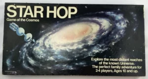 Board game titled "STAR HOP Game of the Cosmos" featuring an artistic depiction of a spiral galaxy and a stylized space probe, with text stating "Explore the most distant reaches of the known Universe. The perfect family adventure for 2-4 players, Ages 10 and up."