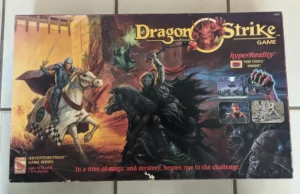 Image of the "DragonStrike" board game box art, featuring a fantasy scene with a knight riding a horse, a dragon, and other mystical creatures, with inset images of gameplay and a label indicating a VHS video inside.