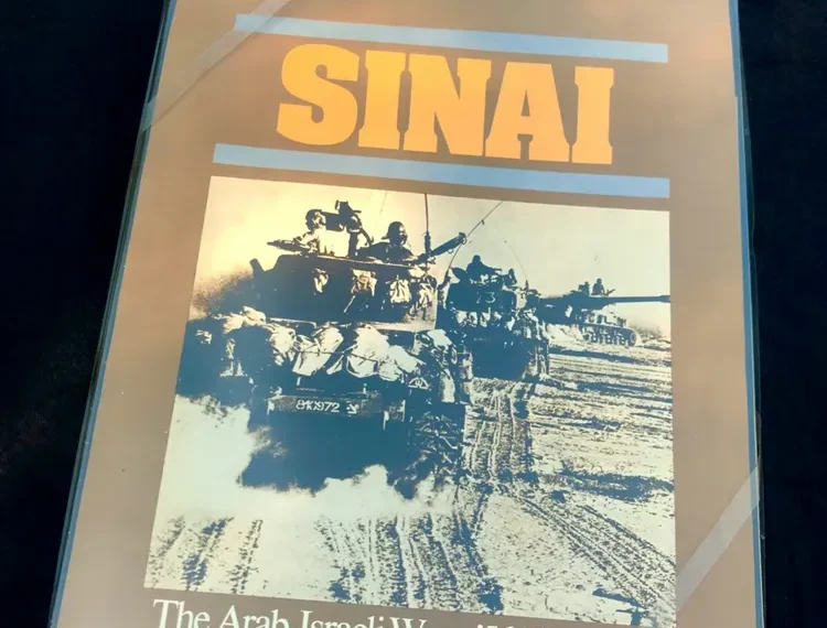 A board game titled "SINAI: The Arab-Israeli Wars: '56, '67 and '73" with an image of a military vehicle and troops on the cover, placed on a dark surface.