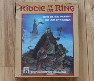 The image shows a worn board game box titled "Riddle of The Ring," which is based on J.R.R. Tolkien's "The Lord of the Rings." The cover art features two characters in a dramatic pose with a foreboding figure and a dark tower in the background. The game is by Iron Crown Enterprises (I.C.E.), described as suitable for beginners as well as experienced gamers, for 2 to 8 players.