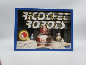 Box cover of the "Ricochet Robots" board game, showing the title with a futuristic font and illustrated robots in a maze-like environment. The box notes a new edition and attributes the design to Alex Randolph, published by Rio Grande Games.