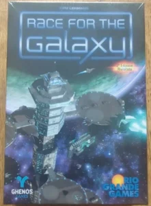An image of a boxed board game titled "Race for the Galaxy" by Tom Lehmann, displaying a space-themed illustration with futuristic spacecraft. The cover includes logos of "Ghenos Games" and "Rio Grande Games" and a text stating "2ª Edizione Rivisitata".