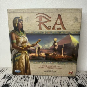 A board game titled "Ra" with ancient Egyptian themed artwork on the cover, including the image of a person dressed as an Egyptian pharaoh, pyramids, and a hieroglyphic border. The text on the box reads "A GAME OF GODS AND GLORY IN ANCIENT EGYPT" and credits "REINER KNIZIA" as the game designer. The publisher's logos, "Euro Classics" and Alea, are displayed in the corners.