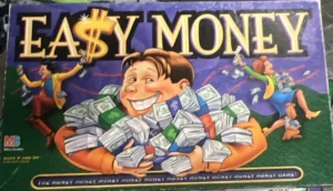 Board game "EASY MONEY" box cover featuring cartoon characters joyfully handling stacks of cash, with the title stylized to emphasize the dollar sign in "EASY." The Milton Bradley logo is visible, and it's for ages 9 and up with a tagline "THE MONEY MAKES IT MOVE...MORE MONEY MORE FUN GAME."