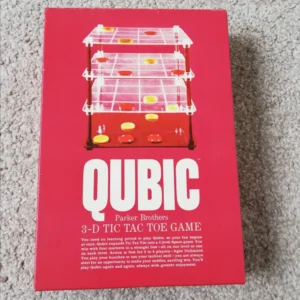 A Parker Brothers "QUBIC 3-D Tic Tac Toe Game" lying on a carpeted floor, showing the box with a clear plastic game board with yellow and red pieces arranged in stacks.
