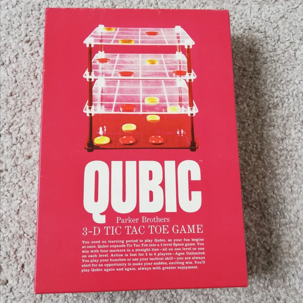 A Parker Brothers "QUBIC 3-D Tic Tac Toe Game" lying on a carpeted floor, showing the box with a clear plastic game board with yellow and red pieces arranged in stacks.