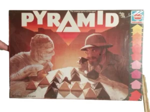 A vintage board game box cover for "PYRAMID" showing an illustration of a mummy and an explorer playing the game with pyramid-shaped pieces, published by Hasbro. Text on the box indicates it is for 2 players, ages 8 to adult.