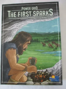 Cover art of "Power Grid: The First Sparks" board game, featuring a prehistoric man creating fire with sparks in a stone setting, overlooking a green landscape with mammoths. The game title and the name "Friedemann Friese" are at the top, while the "Rio Grande Games" logo is at the bottom right.