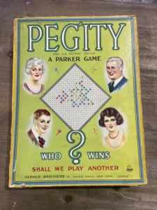 Vintage "PEGITY" board game cover by Parker Brothers, featuring illustrated portraits of two men and two women, a diamond-shaped board layout in the center, and text with game title and "WHO WINS?" question; logos for Parker Brothers and U.S. Patent Office visible.
