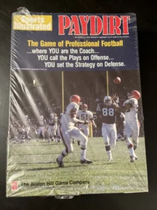 A photo of the cover of "Sports Illustrated PAYDIRT: The Game of Professional Football," featuring an image of football players mid-game with accompanying text and logos.