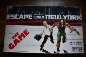 A worn board game box titled "ESCAPE FROM NEW YORK THE GAME," featuring illustrated characters fleeing, with a cityscape in the background. Text on the box indicates it is for 2 to 4 adults, ages 10 and up.